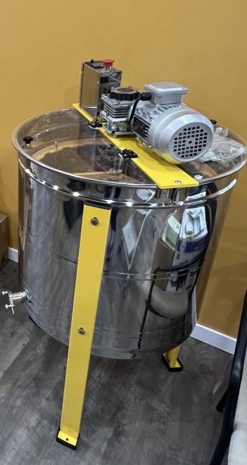 The stainless steel honey extractor on its yellow stand