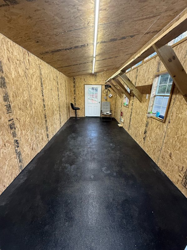 The bare inside of the peafowl house with plywood walls and a black floor
