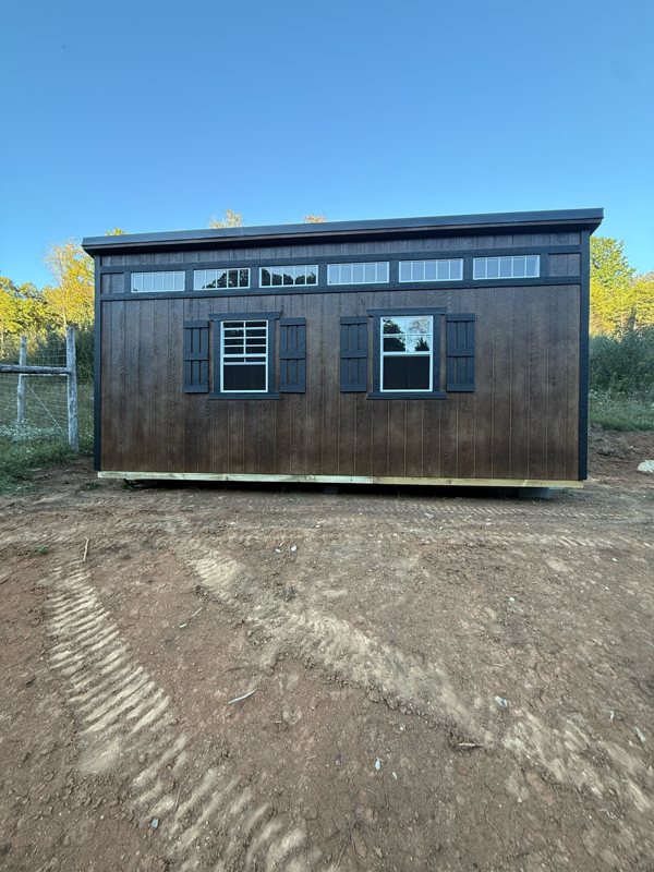The finished dark brown peafowl house with black shutters on a fresh dirt pad